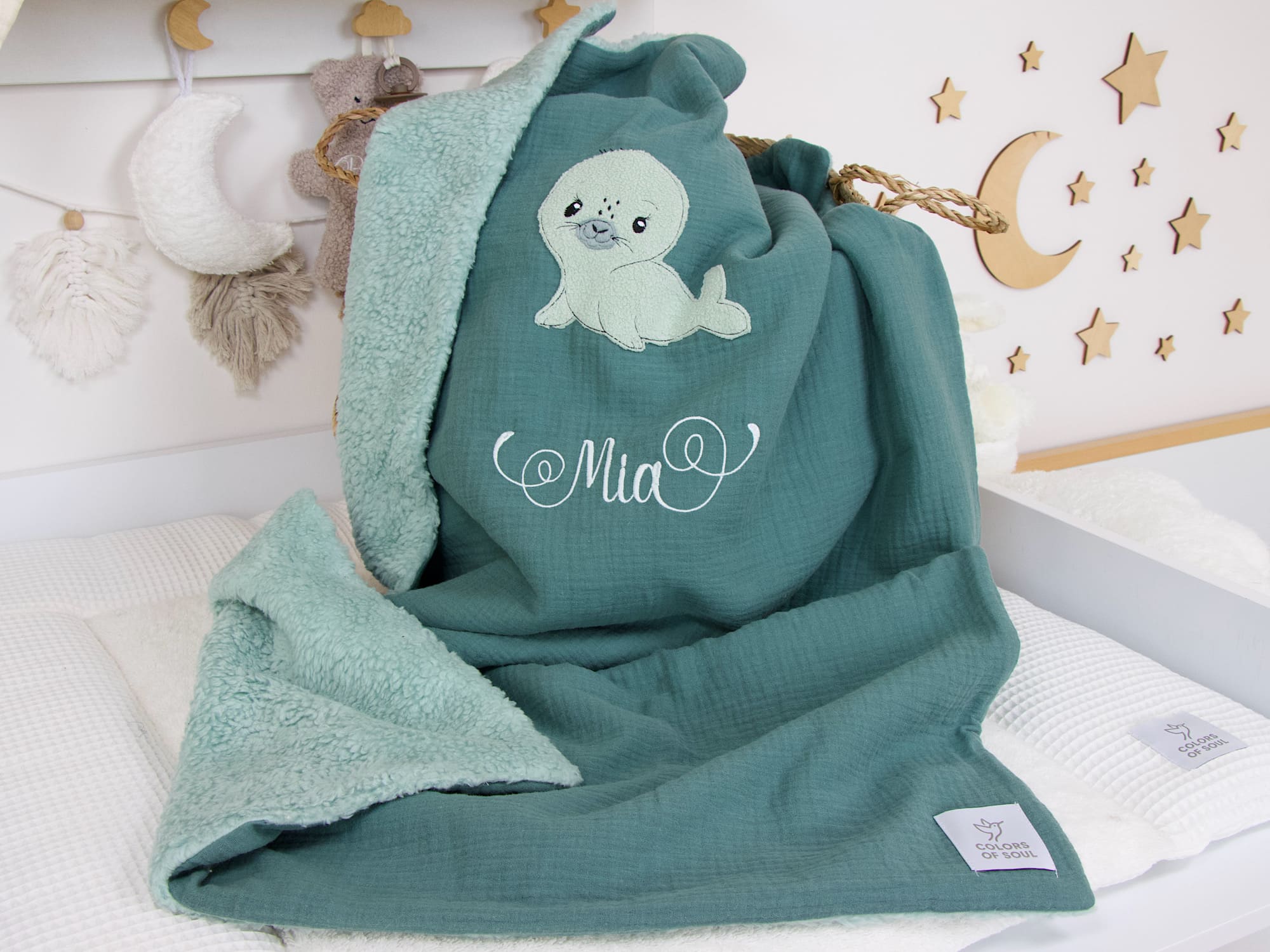 Personalisierte Babydecke in Dunkelmint mit Seehund-Applikation und Namen "Mia", Musselin Dunkelmint außen und Teddyplüsch in Mint innen, aufgefaltet im Babybett