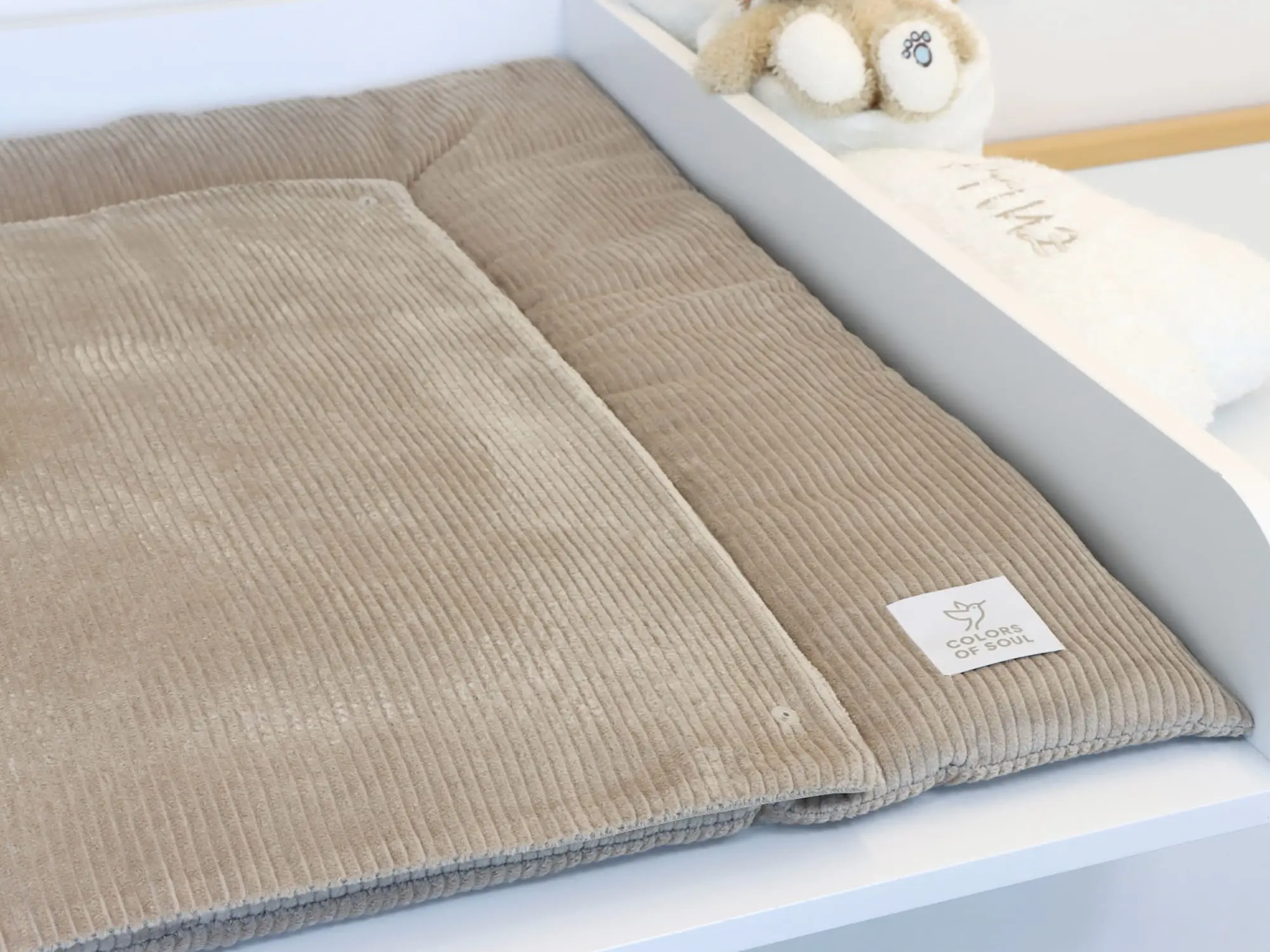 Beige Wickelauflage aus weichem Cordstoff mit passender Wechselauflage für Babys auf weißem Wickeltisch