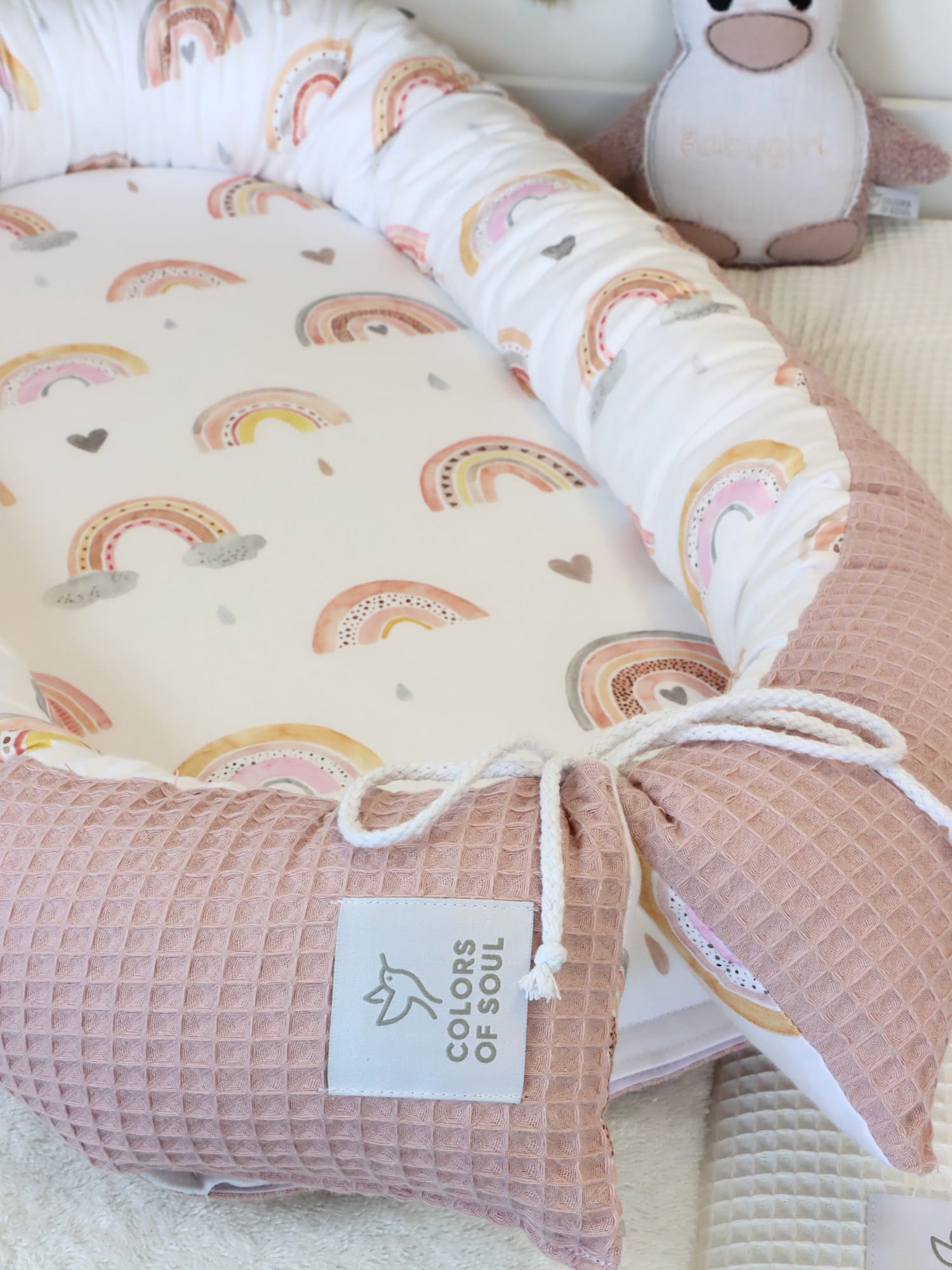Babyzimmer-Szene mit Babynest Regenbogen, rosa Waffelpique und liebevoller Deko.