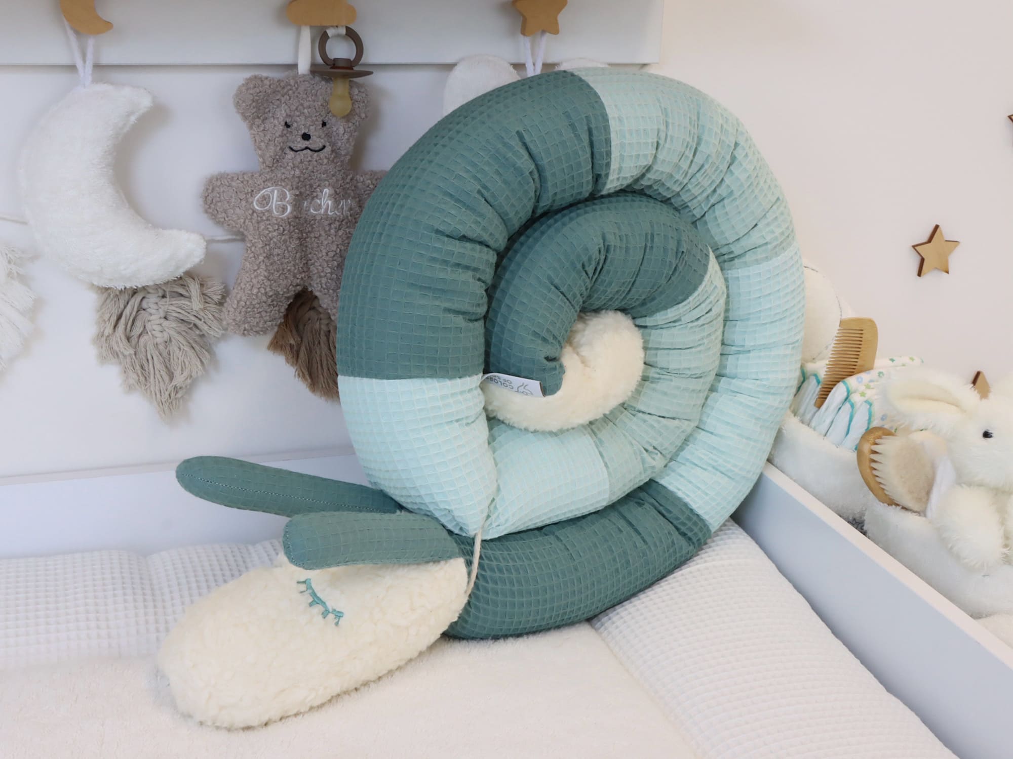 Baby-Bettschnecke aus Waffelpique in sanften Grüntönen, dekorativ eingerollt und mit weichem Teddyplüsch-Kopf im Babybett arrangiert.