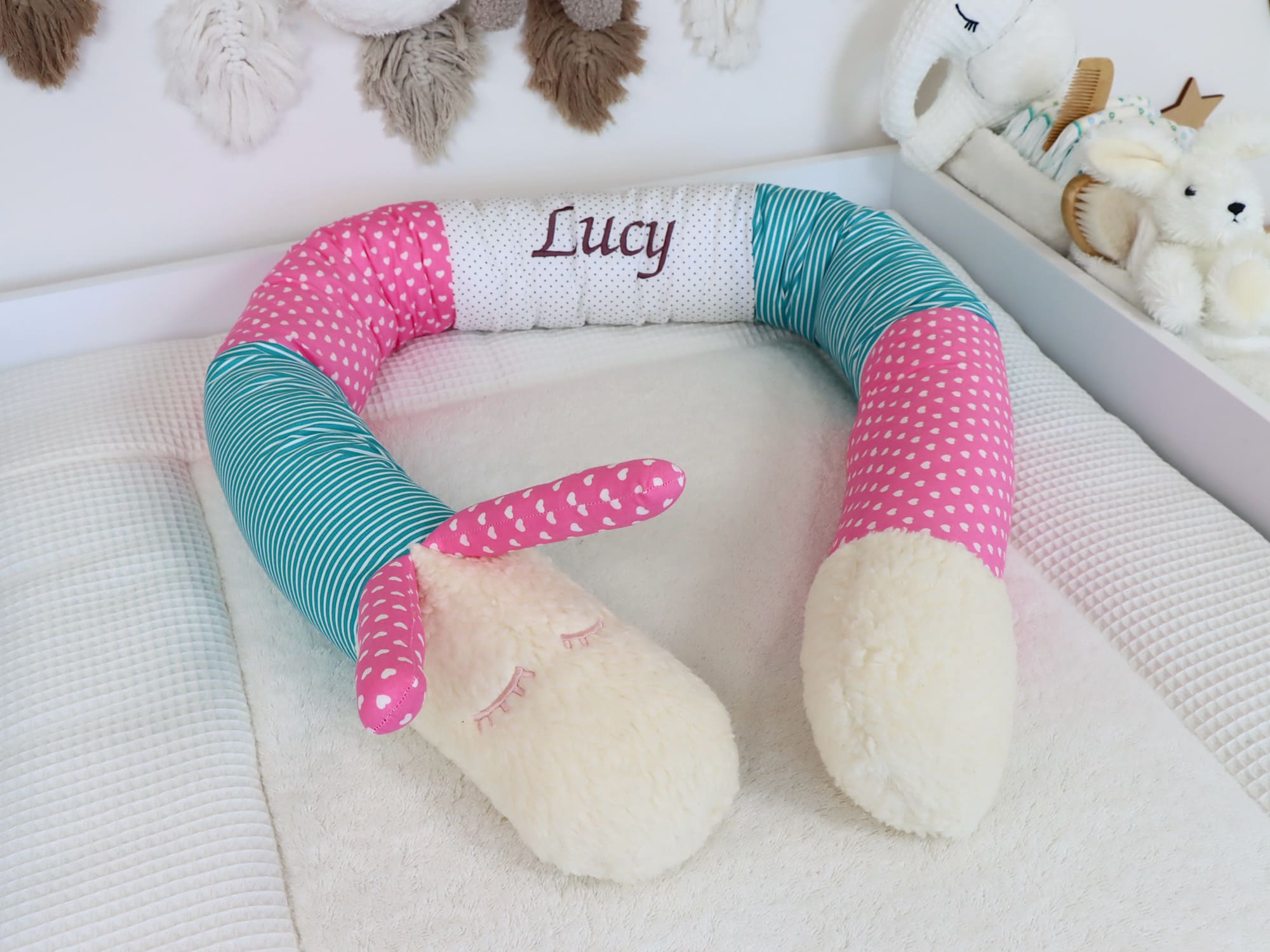 Puckschnecke Türkis Pink Weiß mit Herzchen- und Streifenstoff – personalisiert mit Name Lucy im Babybett