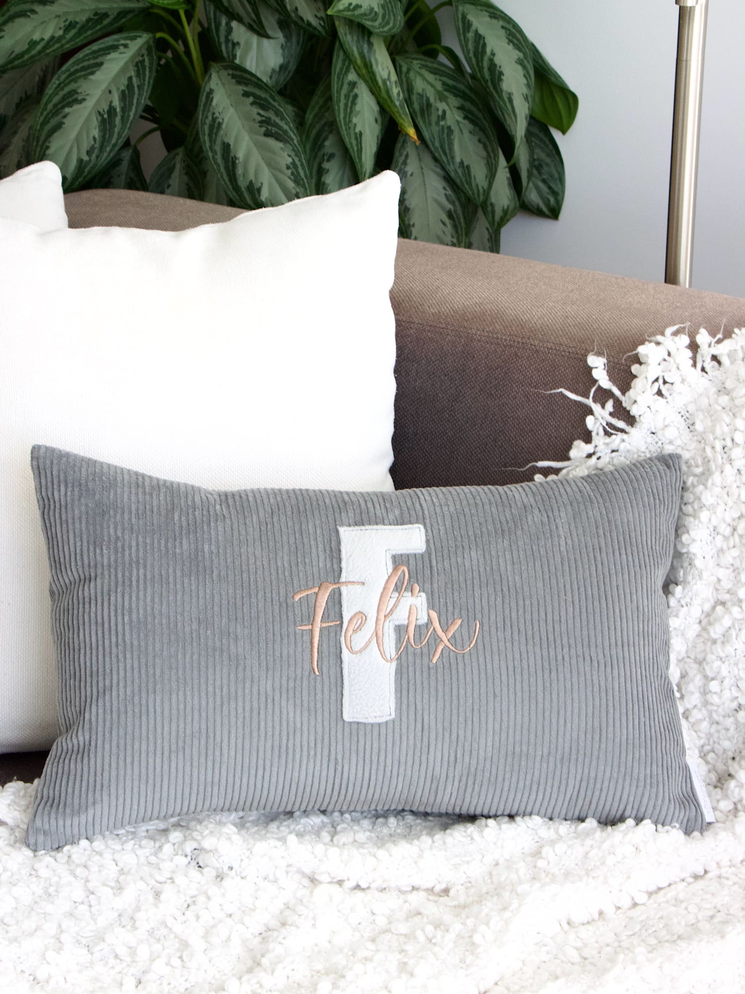 Cordkissen Grau personalisiert auf Sofa – hellgrauer Buchstabe aus Baumwollfleece und Name in Nude