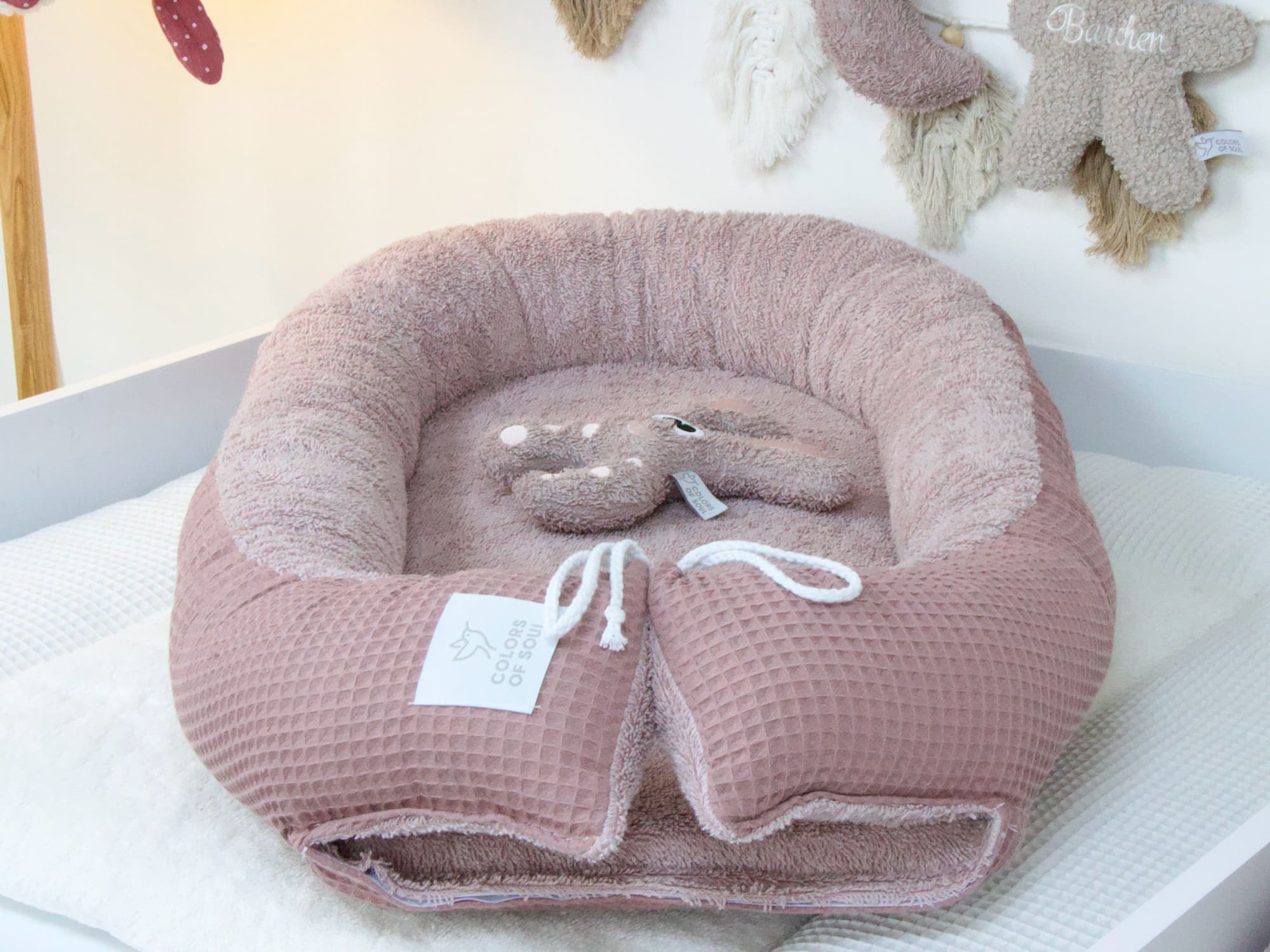 Babynest in Altmalve auf weißer Wickelauflage – stilvoll kombiniert mit Naturtönen und Plüschspielzeug