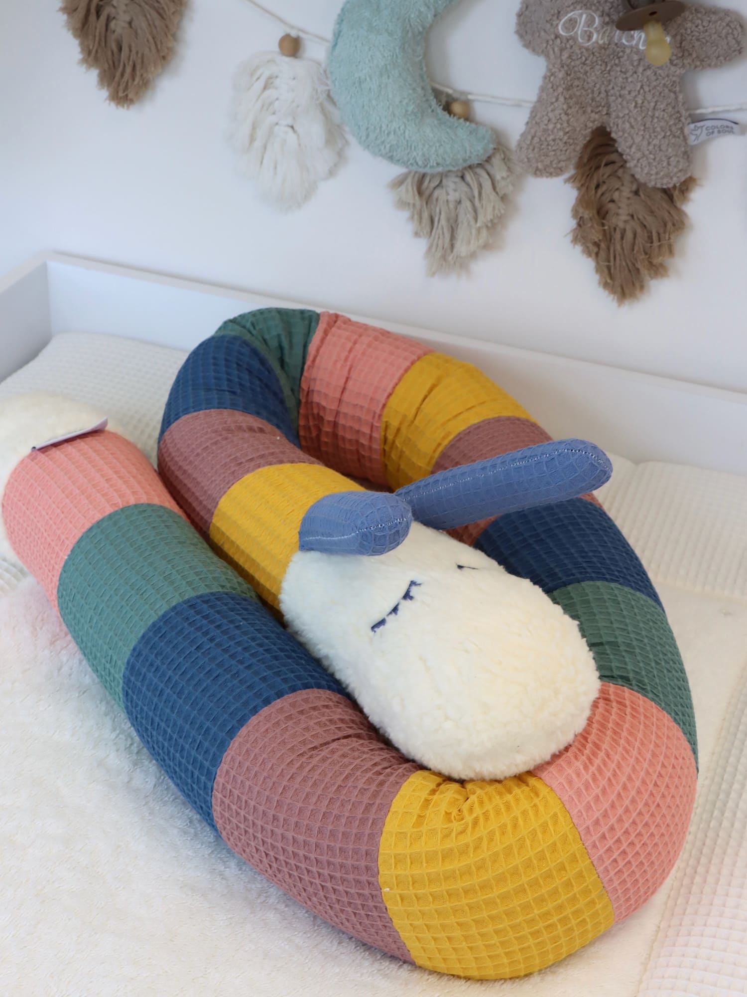 Bunte Puckschnecke Waffelpique mit schlafendem Hasenkopf aus Teddyplüsch auf der Wickelkommode im Babyzimmer.