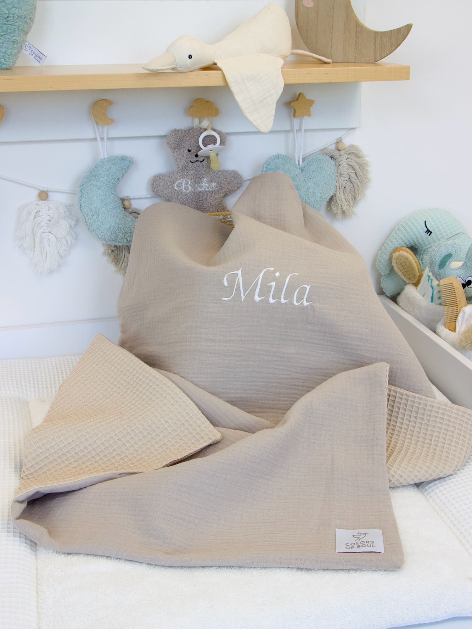 Beige Babydecke aus Musselin und Waffelpique, bestickt mit dem Namen „Mila“, dekorativ im Kinderzimmer präsentiert.