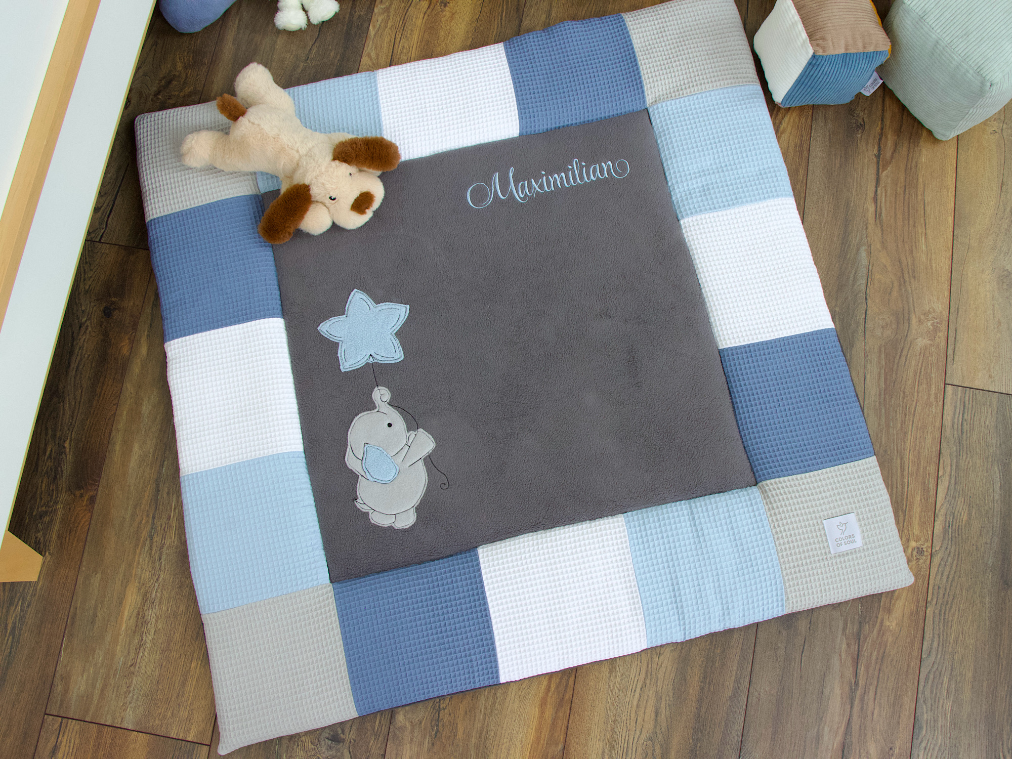 Personalisierte Krabbeldecke im Kinderzimmer mit grauer Liegefläche und blauem Namensstick