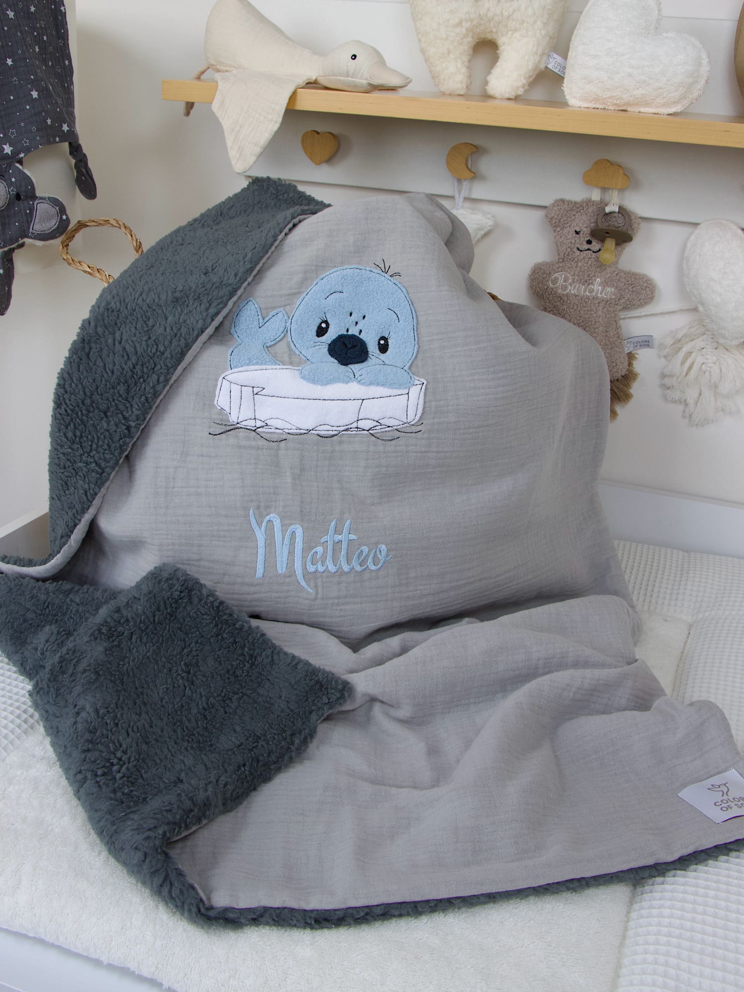 Vorderseite der handgemachten Babydecke in Hellgrau mit blauem Seehund und gesticktem Namen