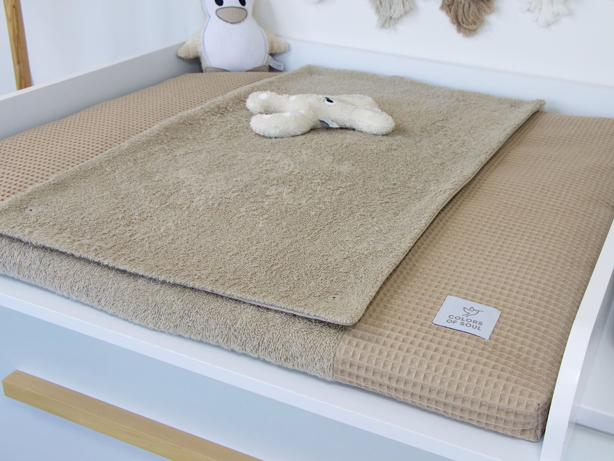 Wickelauflage mit Bezug aus Frottee und Waffelpique in Dunkelbeige auf modernem Wickeltisch – harmonisches Babyzimmer mit Sternen und Kuscheltieren.