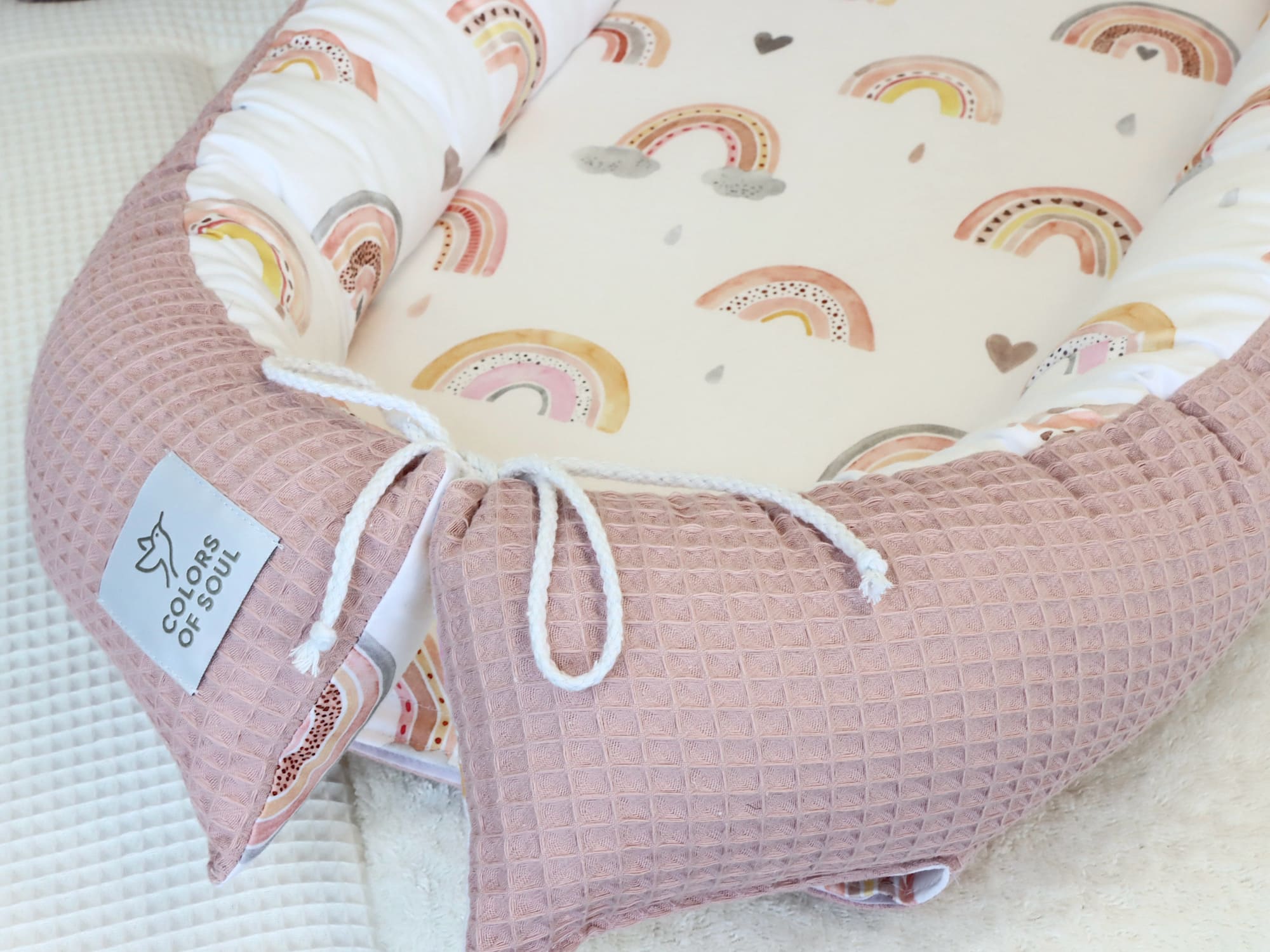 Nahaufnahme Babynest mit Schleifenverschluss aus rosa Waffelpique und Regenbogenstoff.