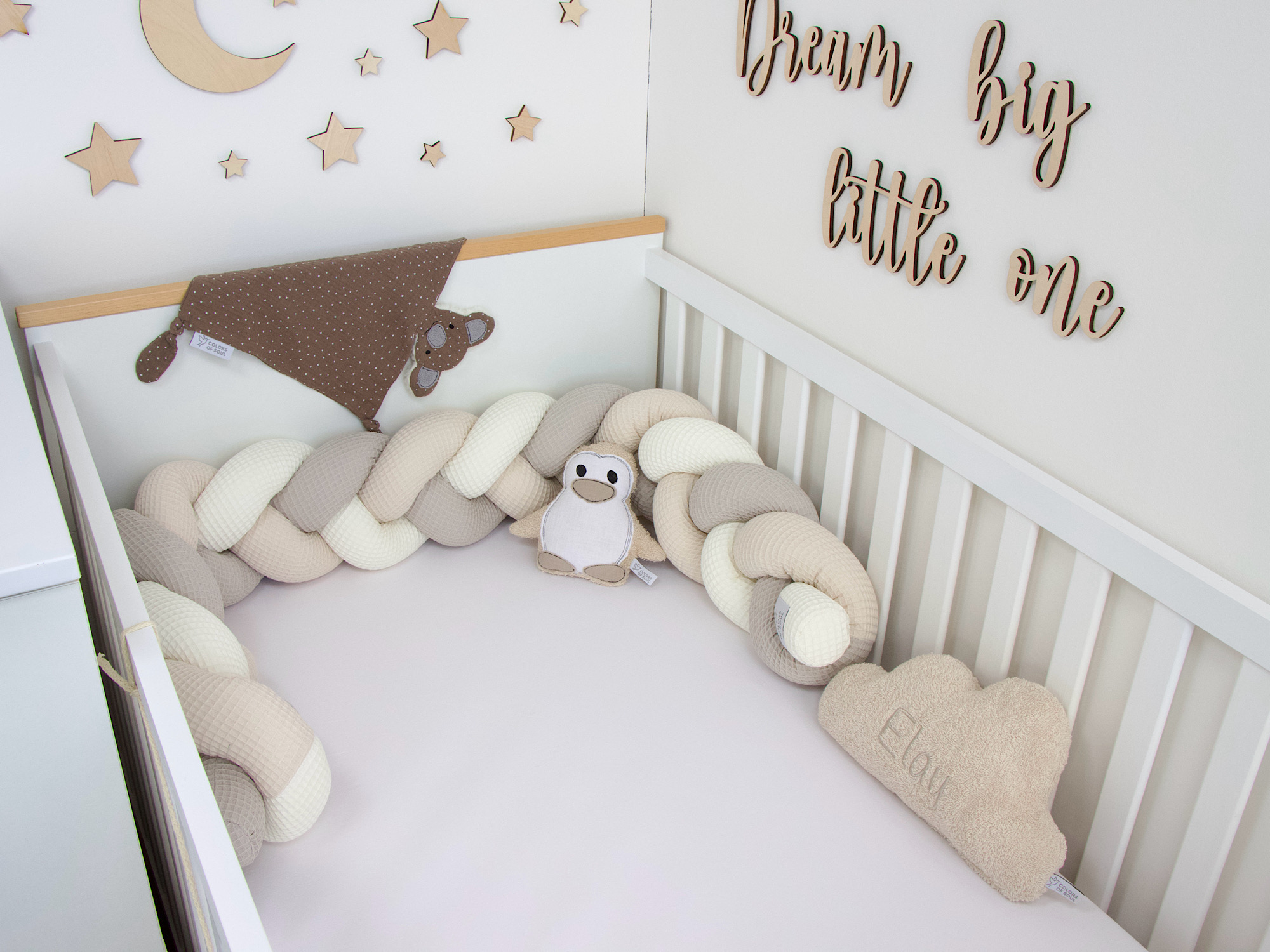 Bettschlange Creme Beige Hellbeige als weiche Umrandung im Babybett mit Deko und Pinguin-Kuscheltier.