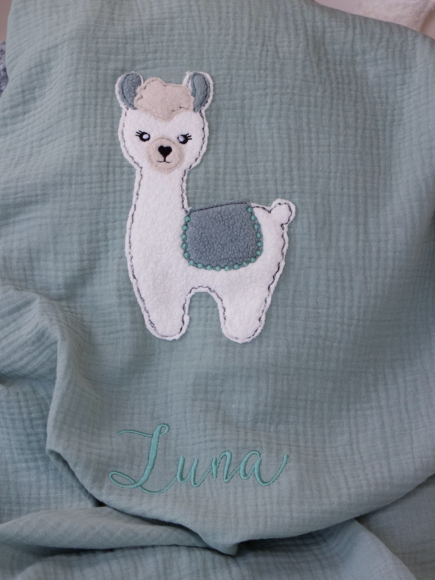 Detailaufnahme der personalisierten Babydecke Hellmint – Lama-Applikation und Namensstickerei Luna.