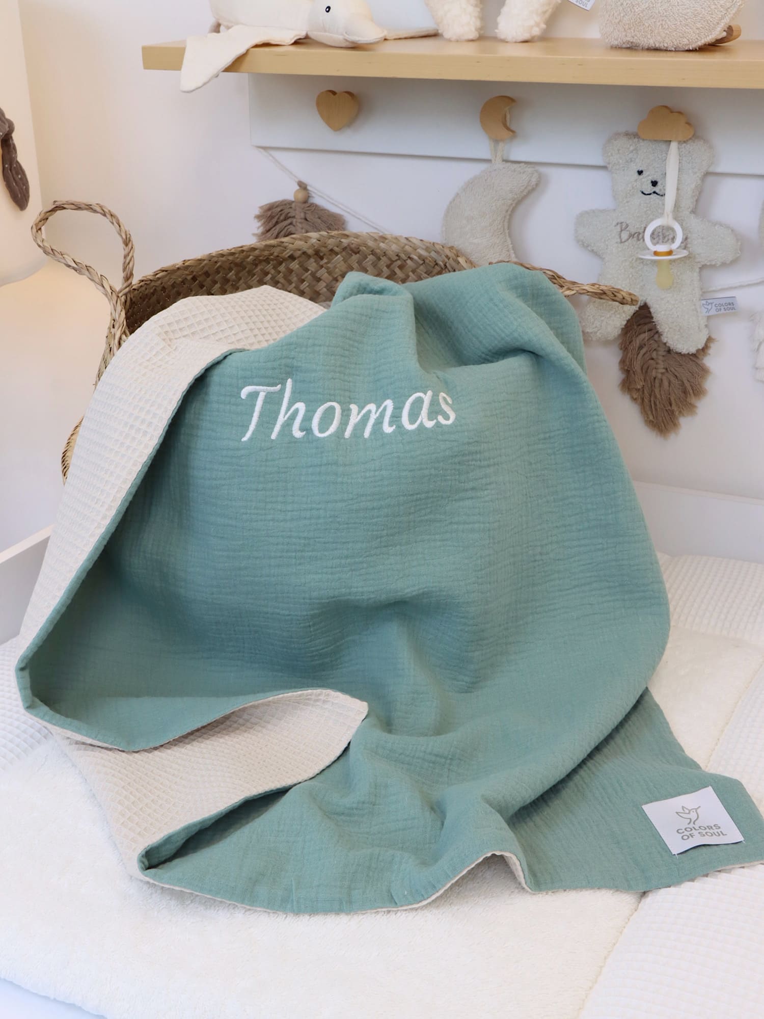 Babydecke Musselin Mint & Waffelpique Hellbeige mit Namensstickerei „Thomas“, liebevoll arrangiert im Kinderzimmer.