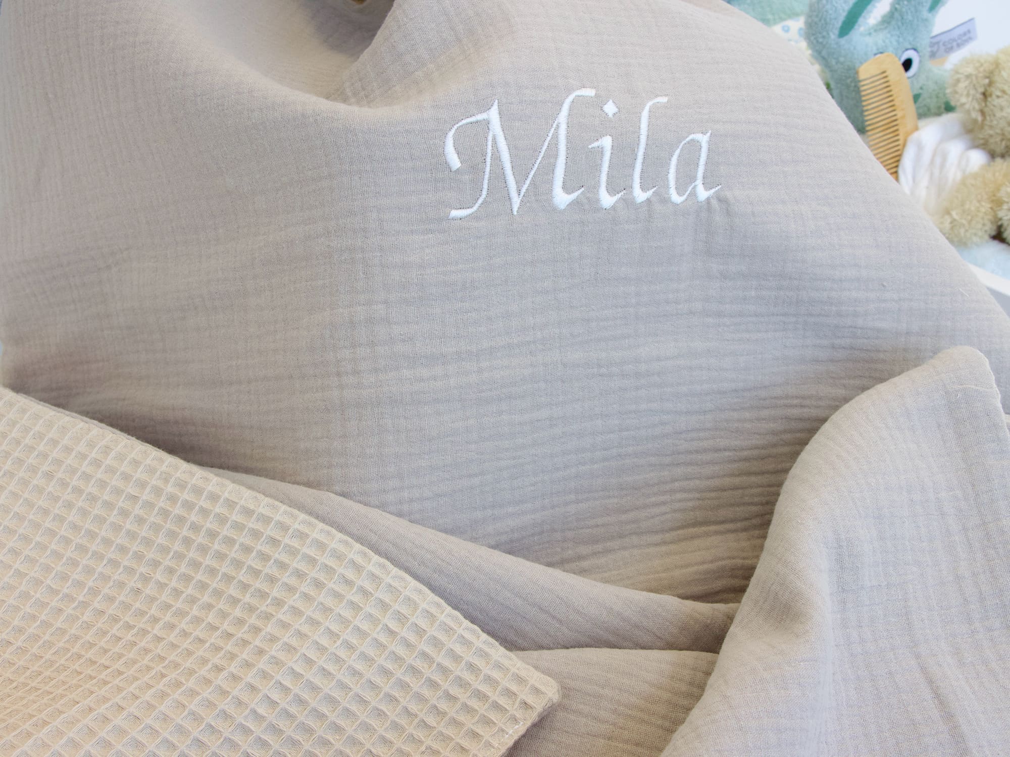 Babydecke aus Musselin Beige und Waffelpique Beige mit Namensstickerei, weich gefaltet auf einer hellen Babybett-Unterlage.
