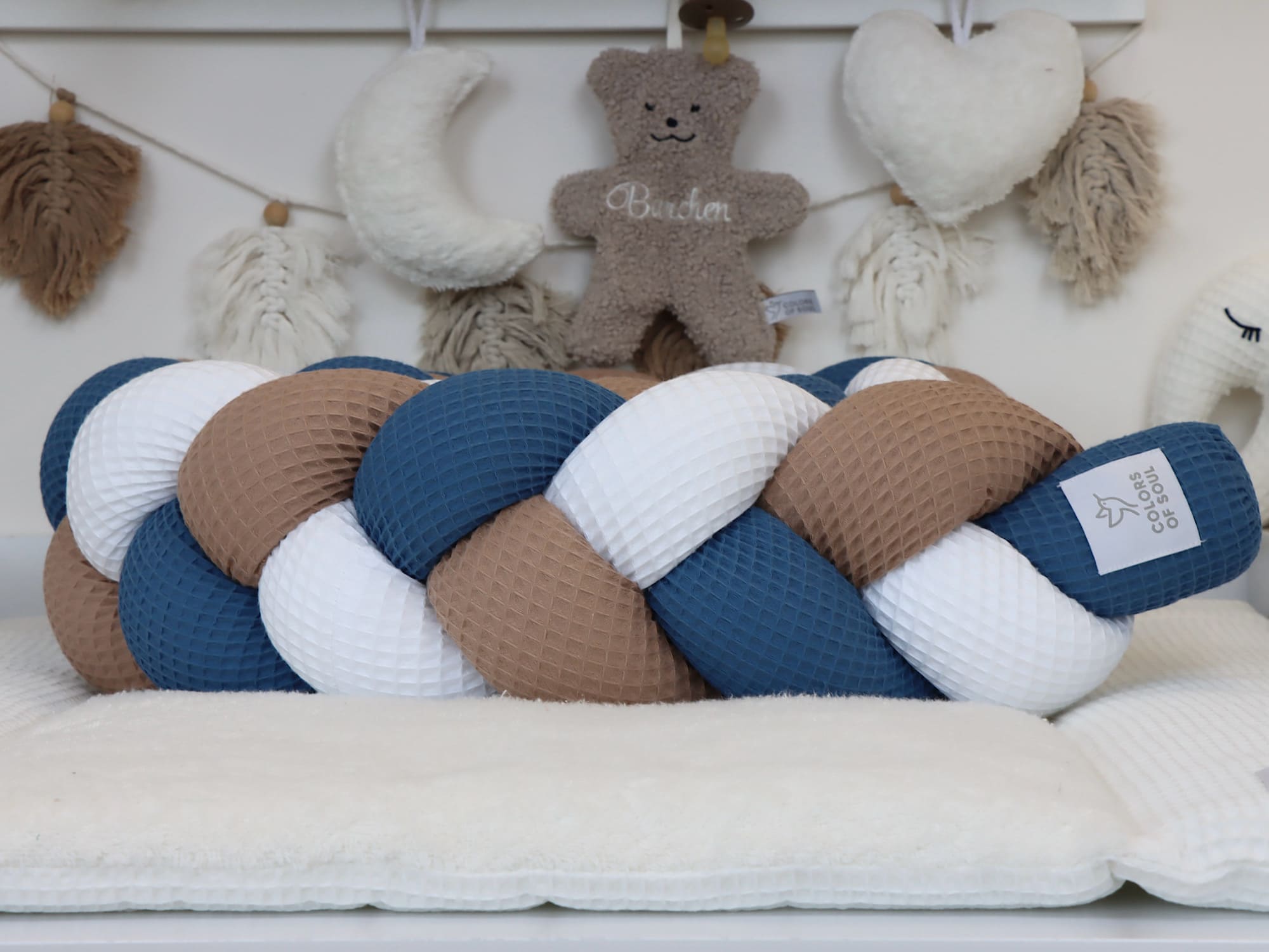 Waffelpique-Bettschlange Weiß–Dunkelbeige–Jeansblau, liebevoll präsentiert auf einer weichen Unterlage im Babyzimmer.