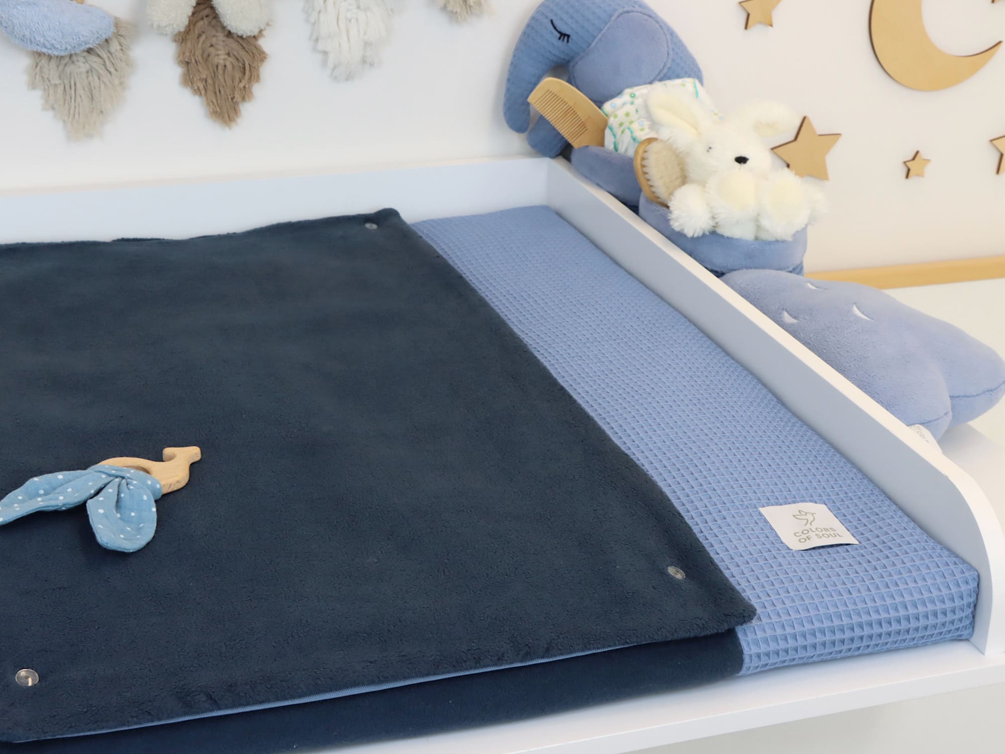 Wickeltisch mit blauer Wickelauflage aus Waffelpique und dunkelblauer Fleece-Auflage, liebevoll dekoriert mit Plüschtieren im Kinderzimmer.