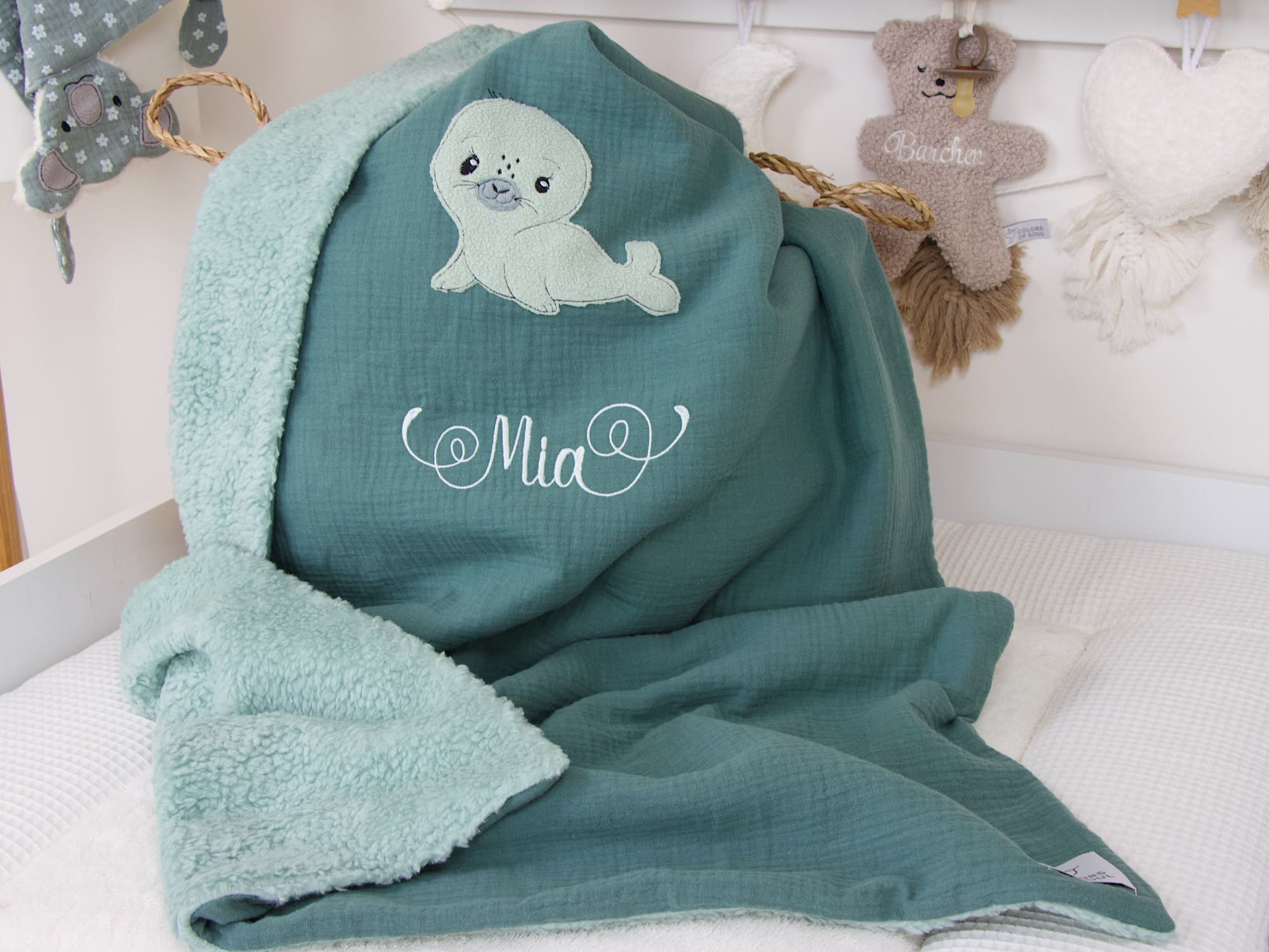 Babydecke Dunkelmint mit Seehund-Applikation und Namen "Mia", aufgelegt im Kinderzimmer, personalisierte Geschenkidee zur Geburt
