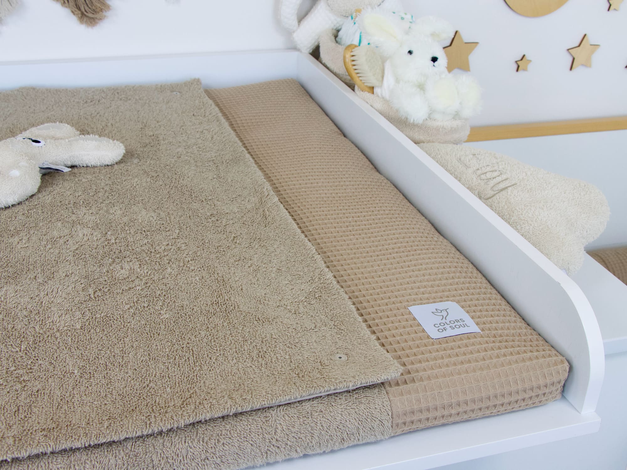 Handgemachte Wickelauflage mit Bezug und Inlett aus Waffelpique und Frottee in Dunkelbeige auf weißem Wickeltisch – stilvolles Babyzimmer mit Kuscheltieren.