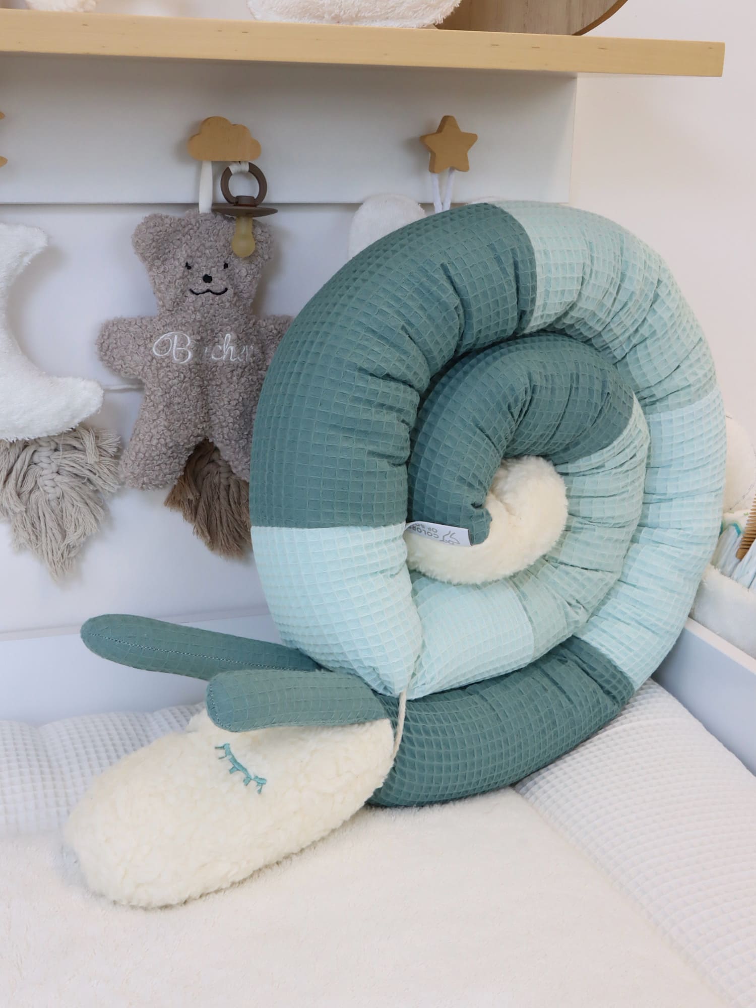 Puckschnecke Baby aus Waffelpique in Altgrün und Mint, hochstehend präsentiert neben Babybett-Deko und Plüschtier.
