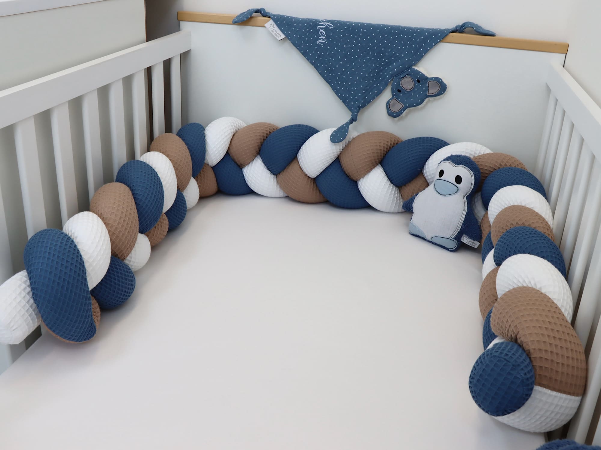 Geflochtene Babybett-Umrandung in Weiß, Dunkelbeige und Jeansblau, seitliche Ansicht mit Kinderzimmerdeko.