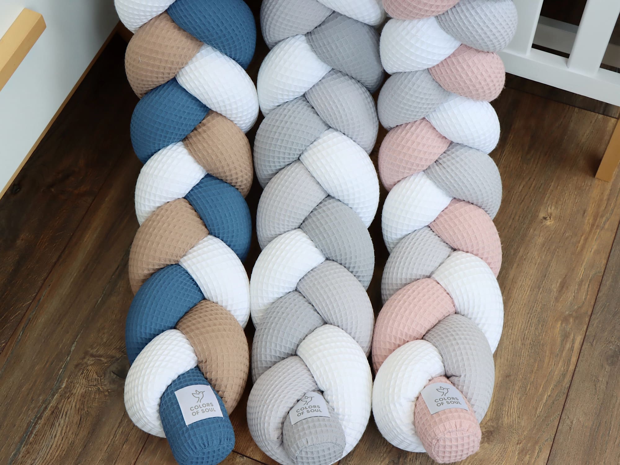 Geflochtene Babybett-Umrandungen aus Waffelpique nebeneinander – Fokus auf Weiß, Dunkelbeige & Jeansblau.