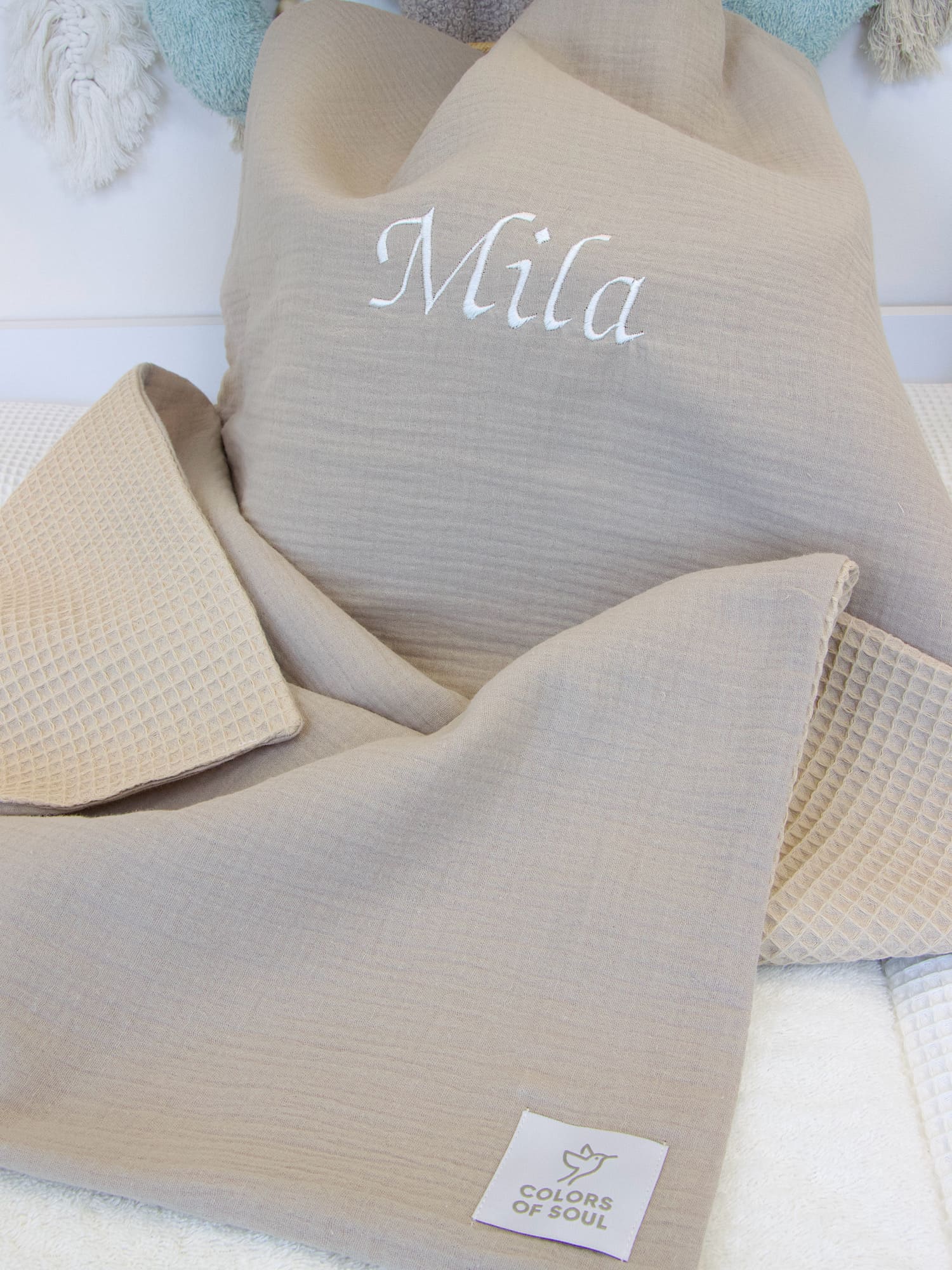 Nahaufnahme der personalisierten Musselin-Beige Babydecke mit dem gestickten Namen „Mila“ und beiger Waffelpique-Unterseite.