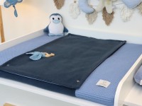 Wickelauflage aus blauem Waffelpique mit dunkelblauem Baumwollfleece auf weißem Wickeltisch, dekoriert mit Plüschtieren und Kinderzimmer-Deko.