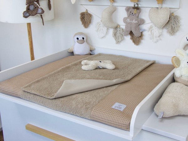 Handgemachte Wickelauflage mit Bezug und Inlett aus Waffelpique und Frottee in Dunkelbeige auf weißem Wickeltisch – stilvolles Babyzimmer mit Kuscheltieren.