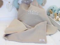 Personalisierte Babydecke aus Musselin Beige und Waffelpique Beige mit Namensstickerei „Mila“, weich drapiert im Babybett.